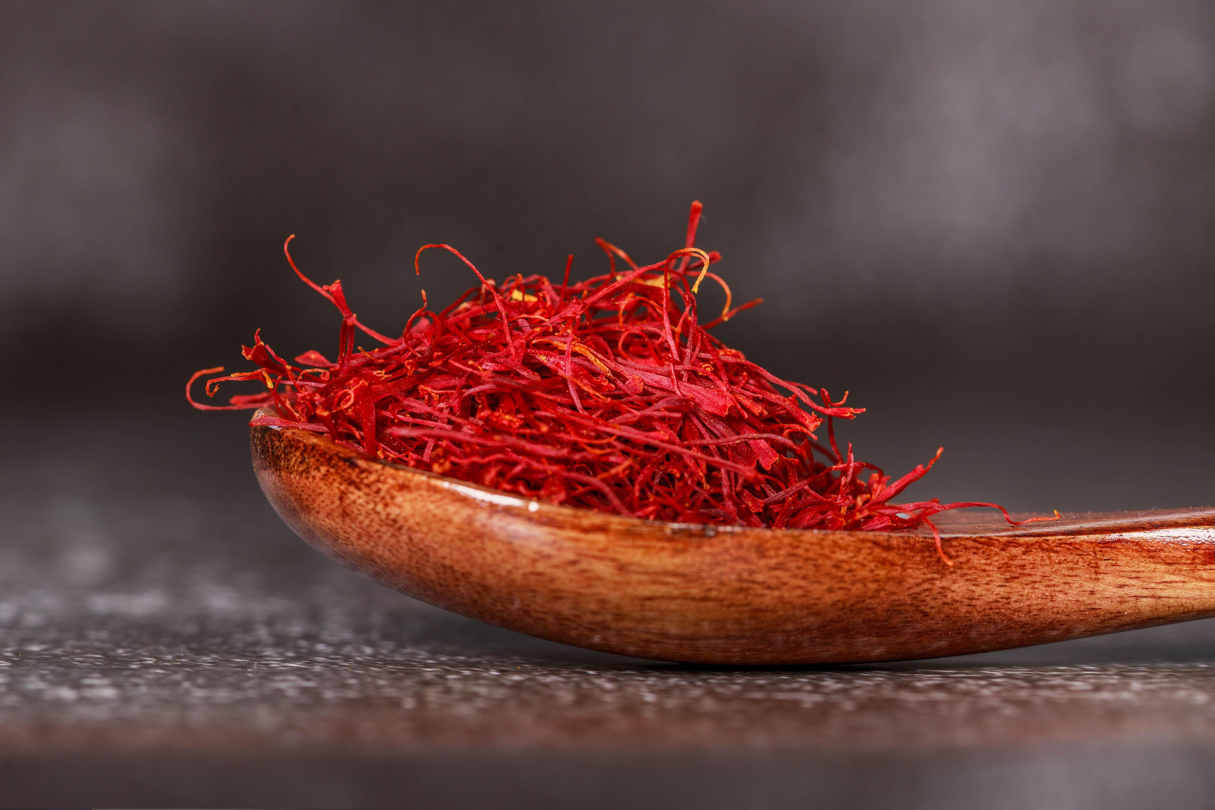 Close up of premium saffron threads in a wooden spoon on a dark surface under dramatic studio lighting.