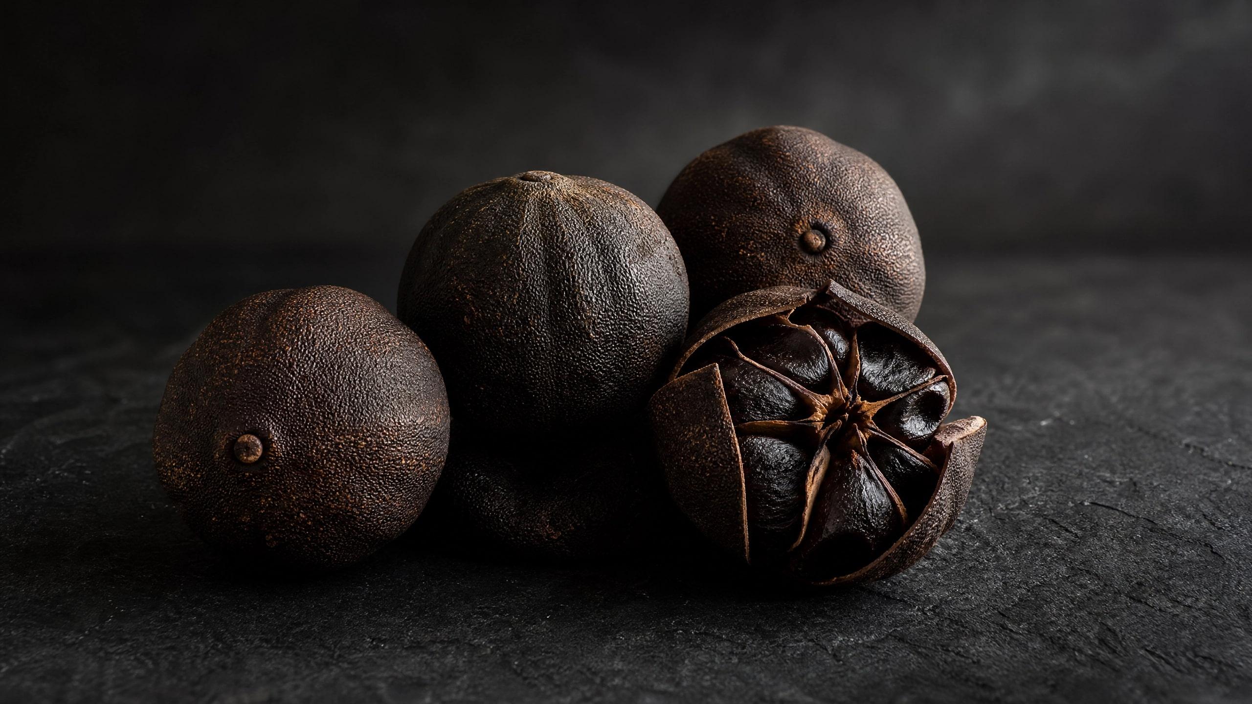 Whole and halved dried black lemons (Loomi) on a dark stone surface.