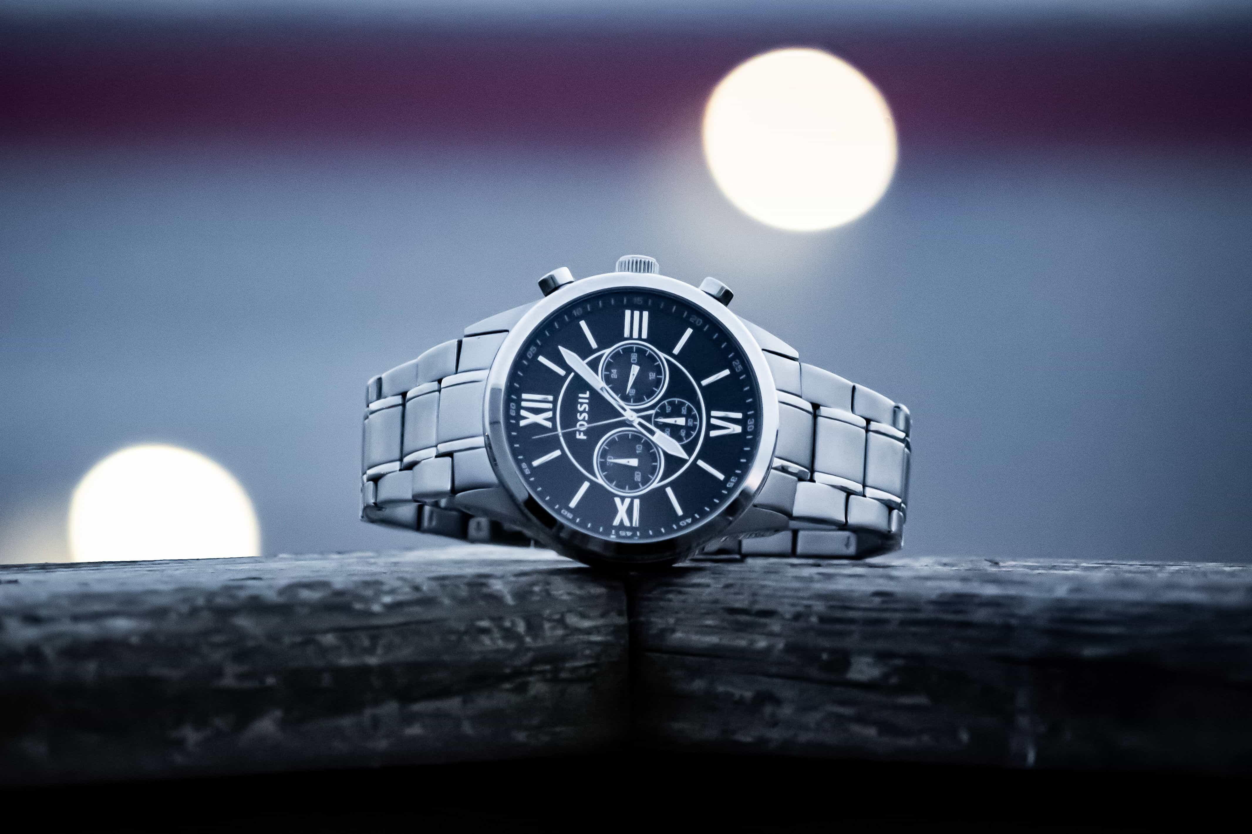 Silver stainless steel wristwatch with a black dial displayed on a wooden surface against a blurred background.