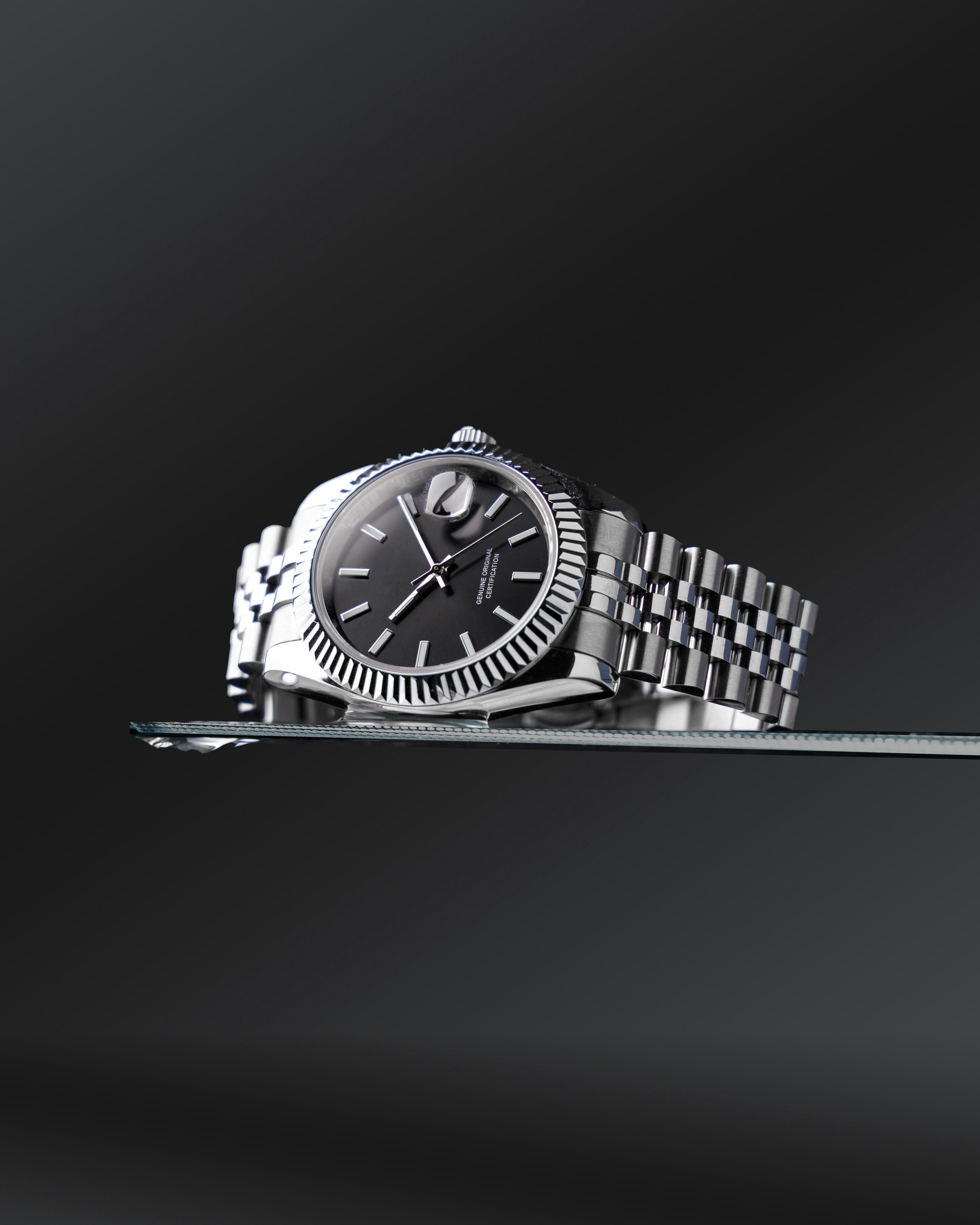 Luxury stainless steel wristwatch with a black dial on a glass display.